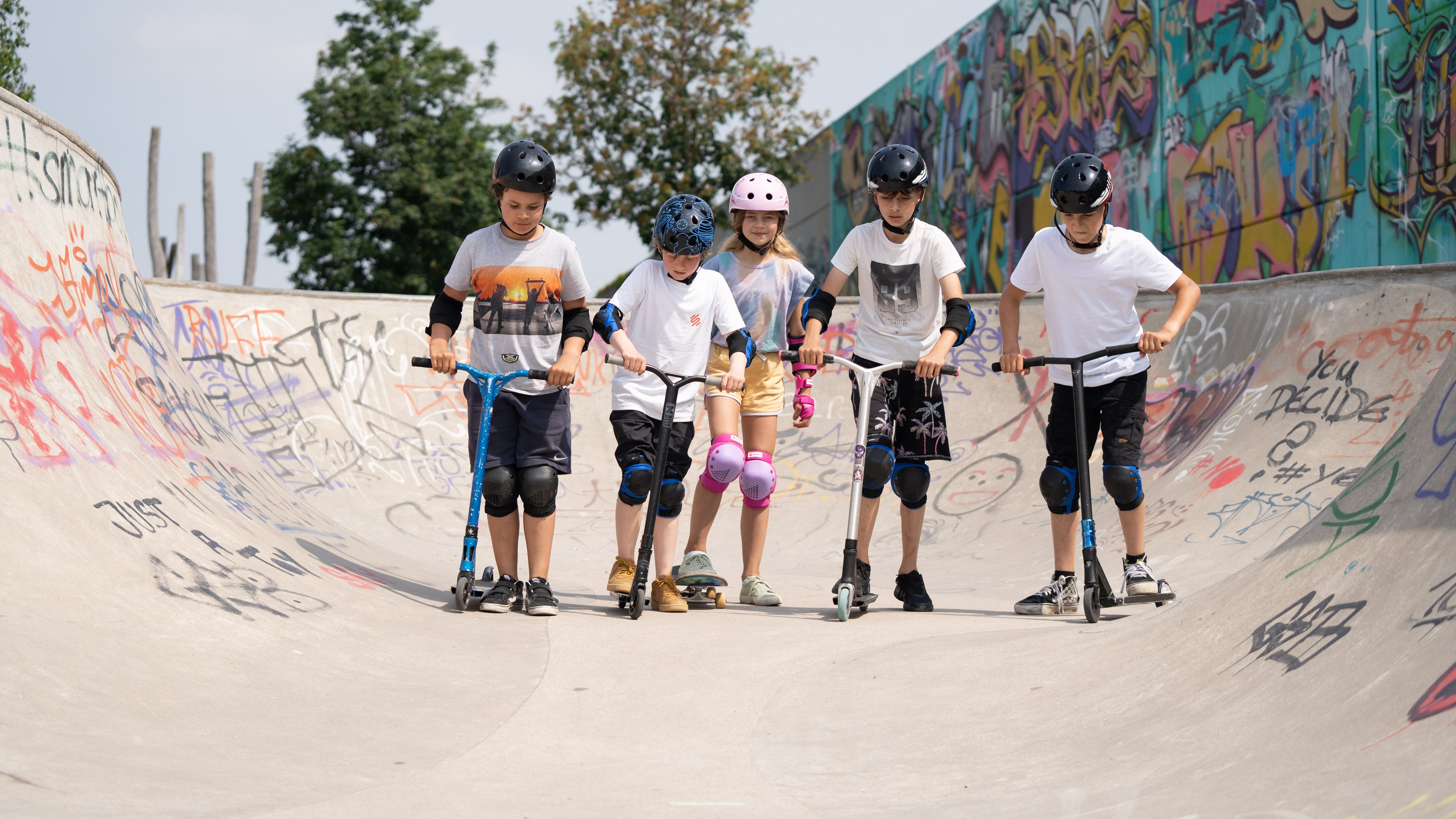 Kinder in einem Skatepark, die Skate-Schutzausrüstung bestehend aus Knieschonern und Ellbogenschonern tragen.