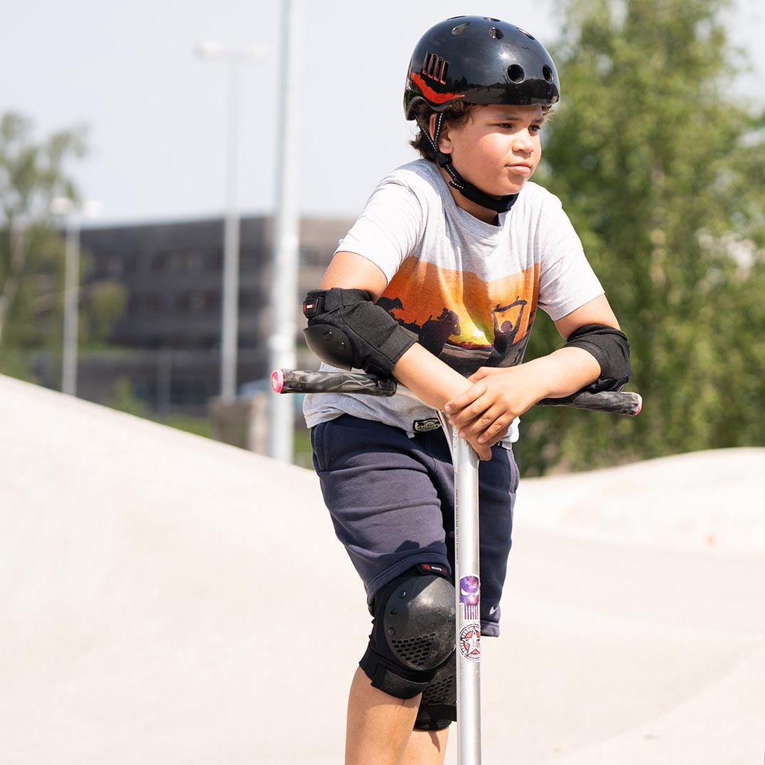 Ein Junge mit einem Scooter steht im Skatepark ausgerüstet mit Skateschutzausrüstung